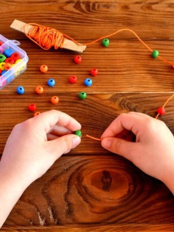 Children hands holding beads and cord. Baby sensory game